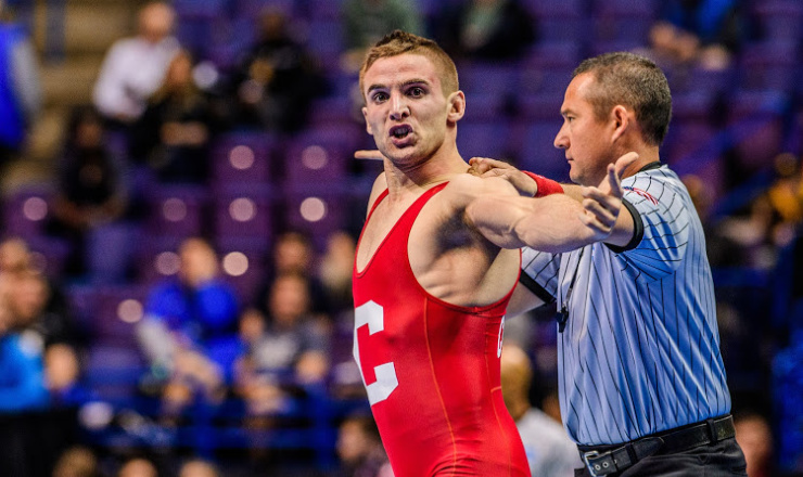 Dylan Palacio in a red Cornell singlet, arm extended, beside the referee during a match